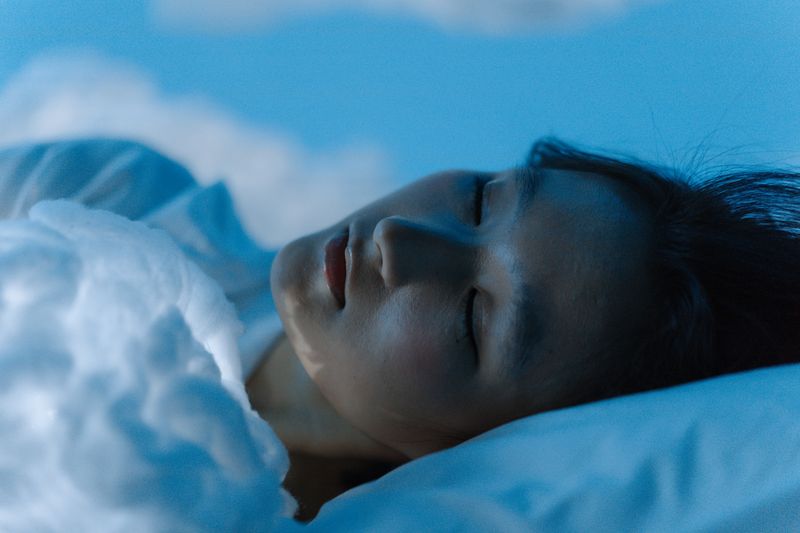 Woman sleeping peacefully in bed under soft blue-toned lighting