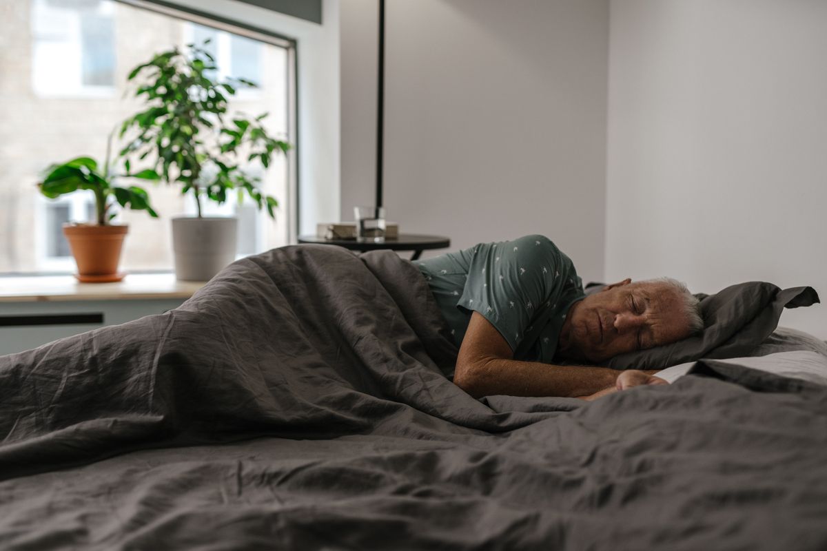 Older person sleeping peacefully in bed under a heavy blanket
