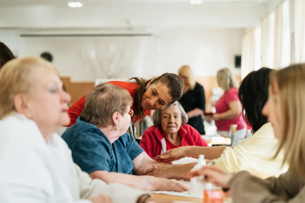 A smiling caregiver warmly engaging with elderly residents at a table in a community center